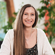 mk-testi - AGP MEDIA Smiling woman with long brown hair wearing a light cardigan, outdoors.